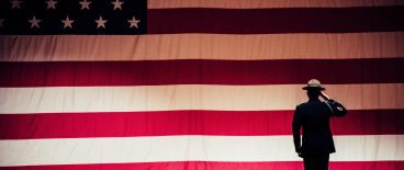 military officer saluting flag with other saluting in audience