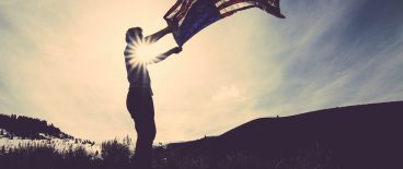Man with American Flag in hands with wind and sun
