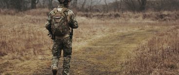 military man hiking through field with gear