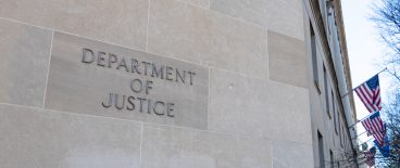 image of the outside of the U.S. Department of Justice building with name on side of building and american flags and trees