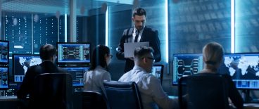 Image of professionals in blue lit room with computer screens and laptops