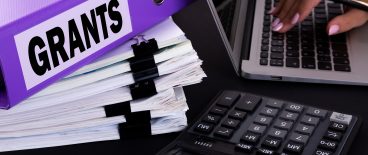 image of large folder labeled Grants, a calculator and laptop with womans hand