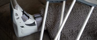 Image of crutches and patient's leg in medical boot under blanket