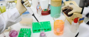 image of gloved lab technicians testing with beakers of colored liquids