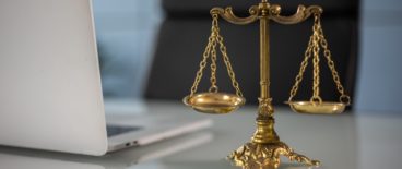 scales of justice sitting on table next to open laptop in front of empty desk chair