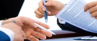close up of two people's hands holding pens and paperwork over a desk