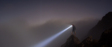 person with a head lamp standing on a cliff looking down