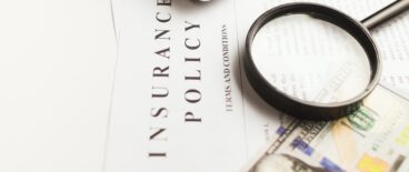 insurance policy document with toy car, money and a looking glass on top of it