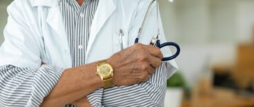 doctor in a lab coat with his arms crossed and stethoscope in one hand