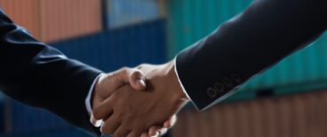 two businessmen shaking hands in front of cargo boxes