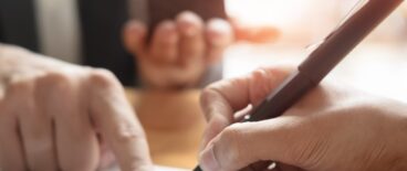 person signing a document with someone pointing for them where to sign