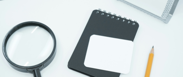 a ruler, looking glass, notepad and a pen on a surface