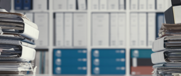 Shelf in the background filled with folders, with a stack of files in front